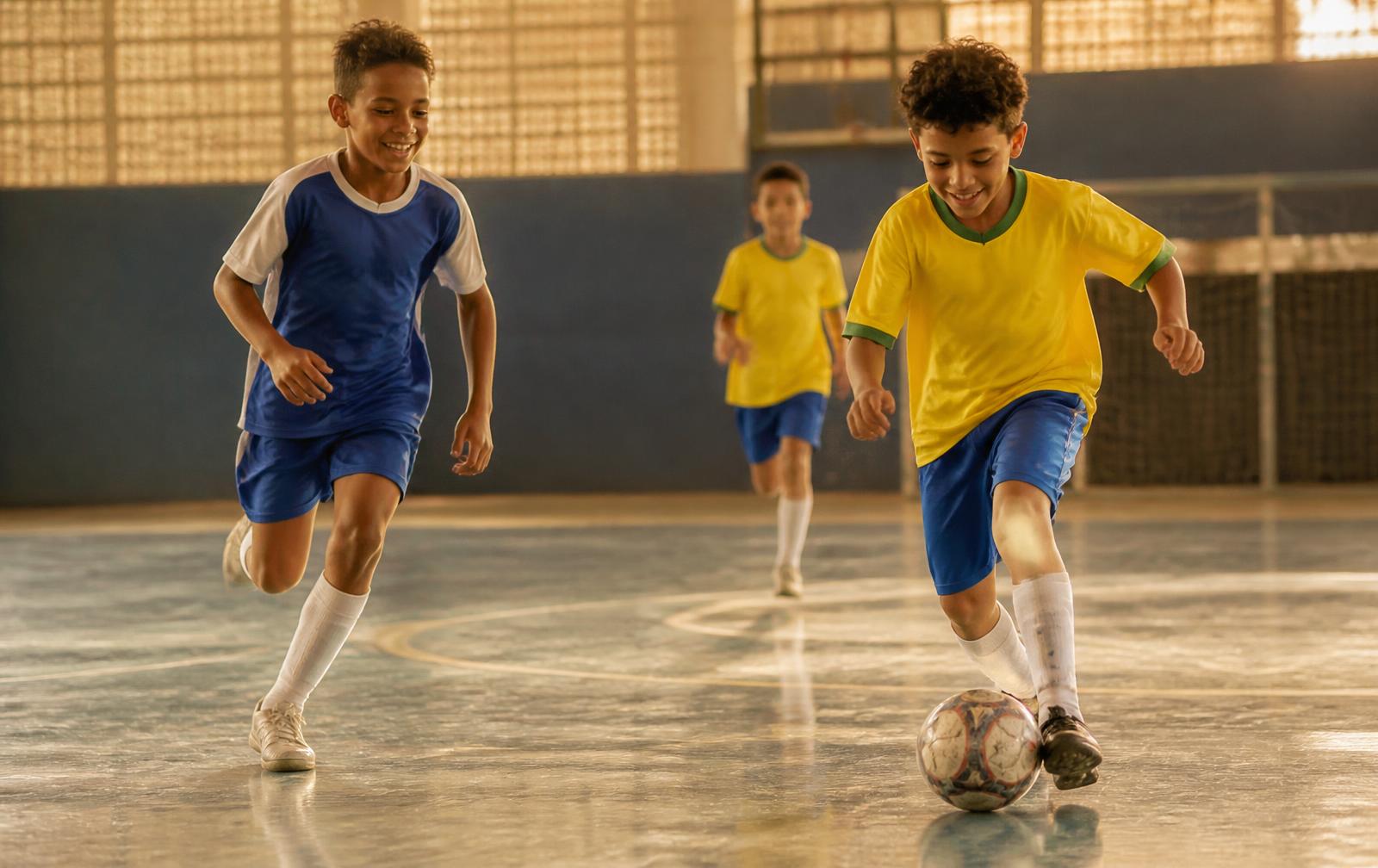 Crianças jogando futsal em quadra coberta